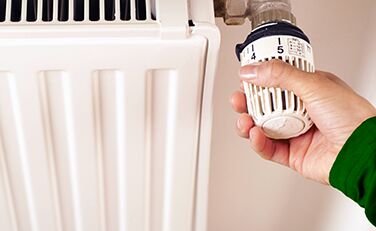 Eine Hand am Thermostat eines Heizkörpers.